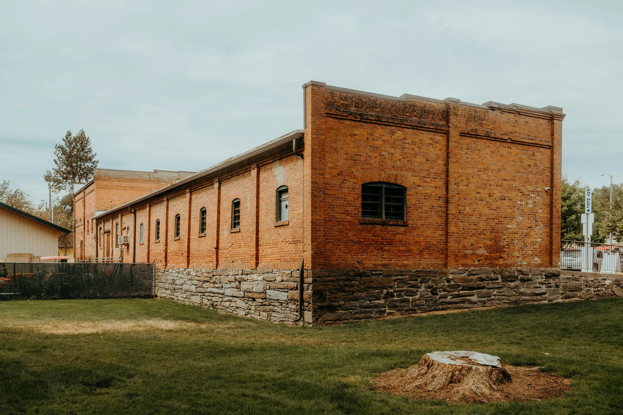 Long brick commercial building with a stone foundation, arched windows, and a paved parking lot with a pay-here sign, the kind of older income property a New York buyer investigates during due diligence