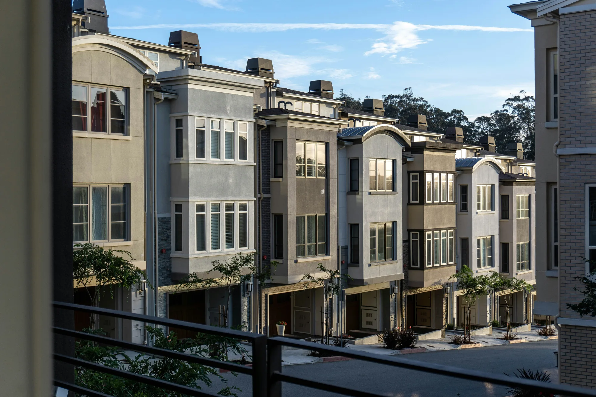 Row of upscale multi-story stucco townhouses with individual attached garages, large windows, and small landscaped entries (representative photo for home inspections in New York County, NY)